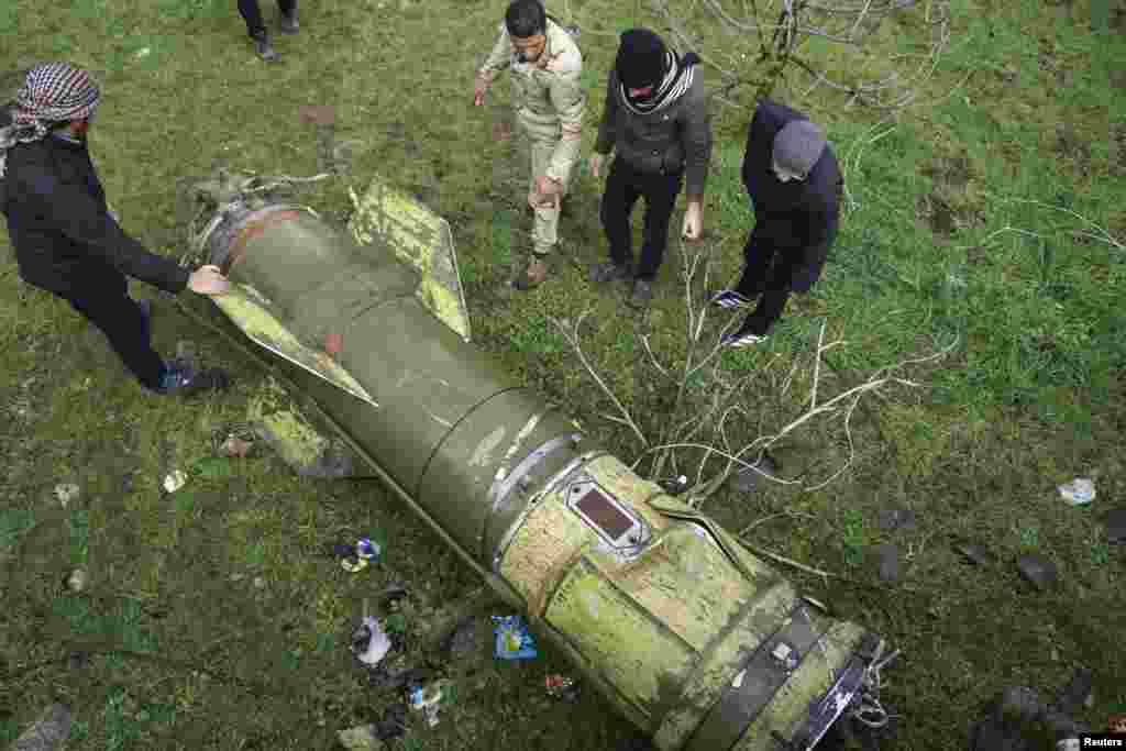 Rebel fighters inspect a piece of a rocket that landed in an area that connects the northern countryside of Deraa and Quneitra countryside, Syria.