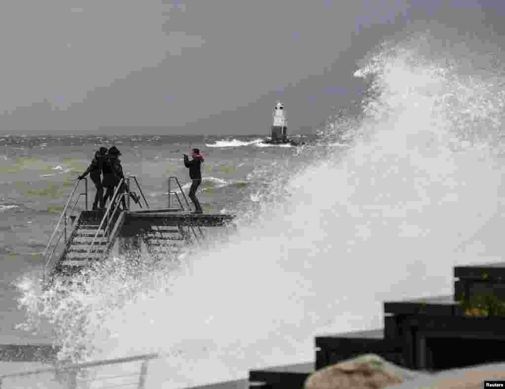 A man takes a photo of his friends posing on a windswept pier in Malmo as a winter storm hit western and southern Sweden.