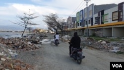 Warga melintas dengan sepeda motor di antara puing-puing dari bekas bangunan yang rusak akibat gempa bumi dan terjangan tsunami di pantai teluk Palu (24/11) Foto: VOA/Yoanes Litha
