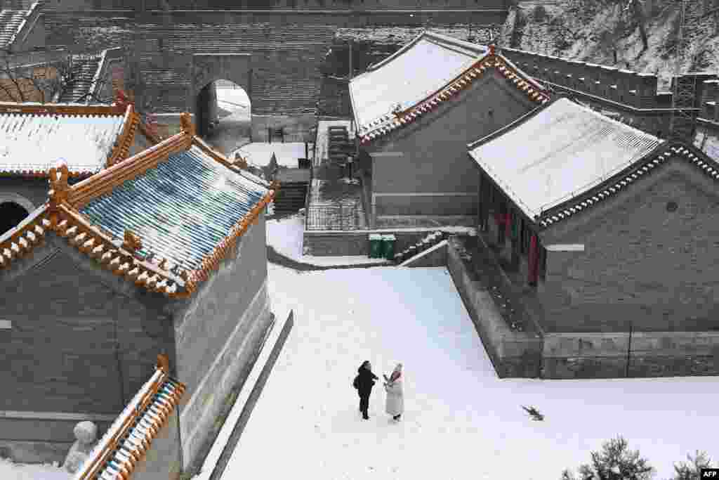 دیوار چین کے قریب بنے رہائشی مکانات کی راہ داریوں میں لوگ برفباری کا لطف لے رہے ہیں۔ ایک خاتون برف سے مجسمہ بنا رہی ہیں۔&nbsp;