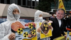 Environmental activists wearing a mask of Japanese Prime Minister Yoshihide Suga and protective suits perform to denounce the Japanese government's decision on Fukushima water, near the Japanese embassy in Seoul, South Korea, Tuesday, April 13, 2021. (AP