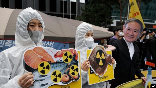 Environmental activists wearing a mask of Japanese Prime Minister Yoshihide Suga and protective suits perform to denounce the Japanese government's decision on Fukushima water, near the Japanese embassy in Seoul, South Korea, Tuesday, April 13, 2021. (AP