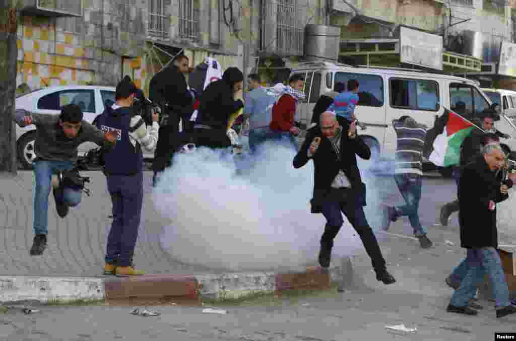 Palestinian protesters run for cover from stun grenades fired by Israeli troops during a protest against the visit of Israeli President Reuven Rivlin to the occupied West Bank city of Hebron.