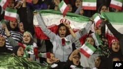 FILE - In this Oct. 16, 2018 file photo, Iranian women cheer as they wave their country's flag after authorities in a rare move allowed a select group of women into Azadi stadium to watch a friendly soccer match between Iran and Bolivia, in Tehran, Iran. 