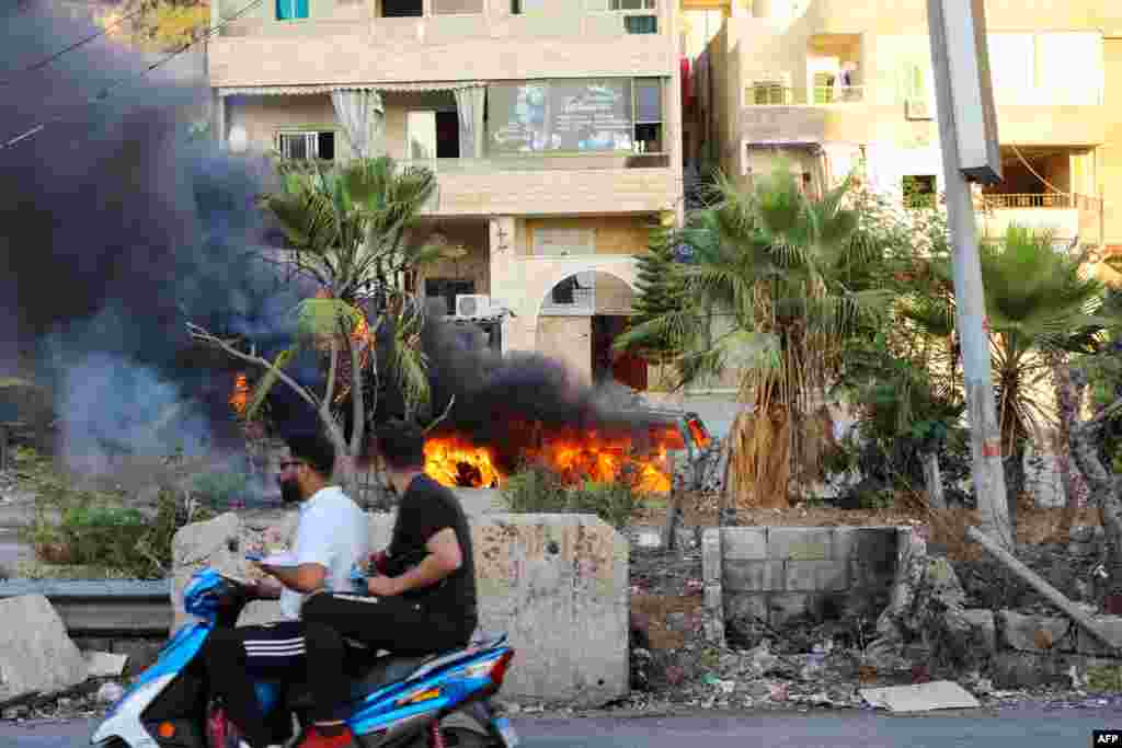 Lebanese men ride a motorcycle past a burning vehicle following clashes in the Khalde area, south of the capital.&nbsp;At least five people including three Hezbollah members were killed when a funeral procession for a party member was ambushed, a Lebanese security source told AFP.