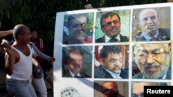 An anti-government protester throws an egg at a poster of Tunisian politicians, including Prime Minister Ali Larayedh (top row, C) and leader of the Islamist Ennahda movement Rached Ghannouchi (center row, R) in Tunis, Oct. 2, 2013.