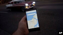 A man holds his phone showing the app "Sube," a ride-hailing app for the aging American sedans on the streets of Havana, in Havana, Cuba, Thursday, Feb. 21, 2019.