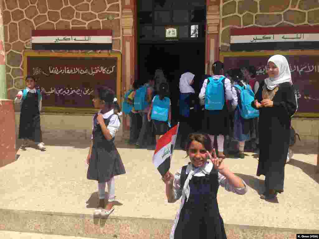 An Iraqi student holds Iraq&rsquo;s flag in one hand and does the V sign with her other hand, Belqis Elementary School (right side of Mosul), July 18, 2017.