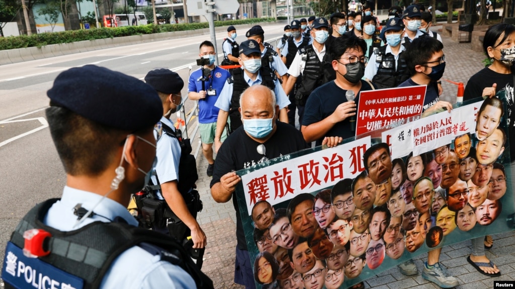 香港支持民主的四名抗议者在中国国庆这一天不惧警察的监视，手举标语牌要求释放政治犯。（2021年10月1日）(photo:VOA)