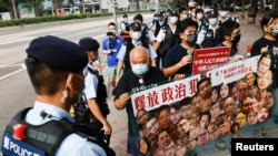 香港支持民主的四名抗议者在中国国庆这一天不惧警察的监视，手举标语牌要求释放政治犯。（2021年10月1日）