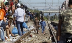Children migrants walk along railway tracks while police officers try to secure the entrance of the railway station in the southern Macedonian town of Gevgelija, as migrants prepare to board a train toward Serbia, Aug. 17, 2015.