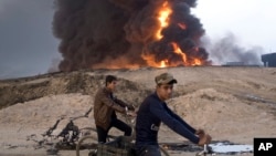 FILE - Young Iraqis ride bicycles next to a burning oil well in Qayyara, about 50 kilometers (30 miles) south of Mosul, Iraq, Oct. 23, 2016. The Islamic State group has launched diversionary attacks. Last week’s assault on Kirkuk offers a glimpse at the kind of response it might mount as Iraqi forces close in on Mosul.