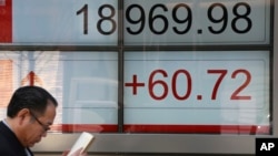 A man walks by an electronic stock board of a securities firm in Tokyo, April 3, 2017. Asian markets were mostly higher Monday, cheered by a positive report on the Japanese economy.