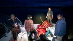 The Stevens family hunting party reacts as a boat pulls into camp just after nightfall with a fresh moose kill, Sept. 15, 2021, near Stevens Village, Alaska. The Yukon River becomes treacherous to navigate a night.