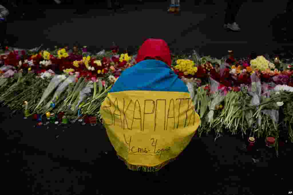 An anti-Yanukovych protester, wearing a Ukrainian flag with the name of his village written across it, places flowers at a memorial for the people killed in clashes in Kyiv's Independence Square, Feb. 25, 2014. 