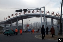 In this Dec. 5, 2018, photo, residents past by the entrance to the "Hotan City apparel employment training base" where Hetian Taida has a factory in Hotan in western China's Xinjiang region.