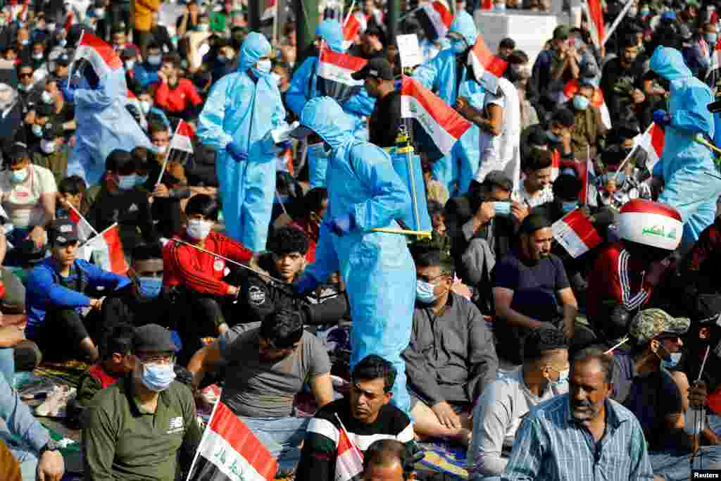 A volunteer wearing a protective suit sprinkles disinfectant as supporters of Iraqi Shi'ite cleric Moqtada al-Sadr attend Friday prayers ahead of a rally in support of al-Sadr at Tahrir Square in Baghdad, Iraq November 27, 2020. REUTERS/Khalid al-Mousily