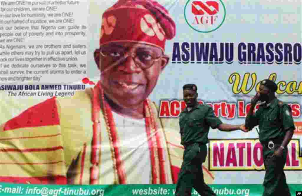 Environmental officials walk past a poster of Bola Tinubu, the leader of the newly formed All Progressive Congress party during the party convention in Lagos, Nigeria, Thursday, April 18, 2013.