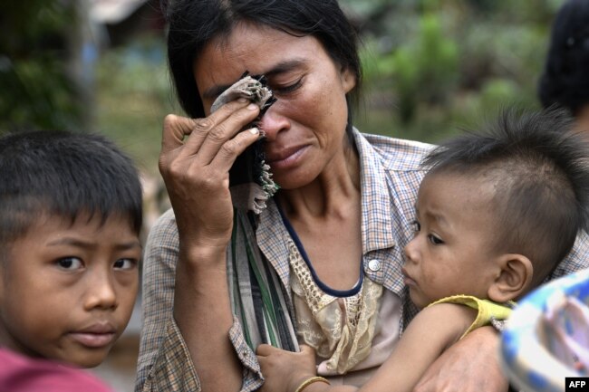 ແມ່ຍິງຄົນນຶ່ງທີ່ອູ້ມລູກຂອງລາວໃນບ້ານແຫ່ງນຶ່ງທີ່ຖືກນໍ້າຖ້ວມຢູ່ເມືອງ ສະໜາມໄຊ, ແຂວງອັດຕະປື, 26 ກໍລະກົດ 2018.