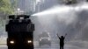 Una manifestante chilena levanta sus brazos en desafío de un cañón de agua de los militares que intentan mantener vigente un estado de emergencia para poner fin a las protestas que han dejado ya 18 muertos. 