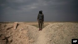 A U.S.-backed Syrian Democratic Forces (SDF) fighter stands atop a hill in the desert outside the village of Baghouz, Syria, Thursday, Feb. 14, 2019. 