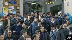 Palestinian police officers block the entrance to the Al-Jazeera TV office, after protesters vandalized it, in the West Bank city of Ramallah, 24 Jan 2011