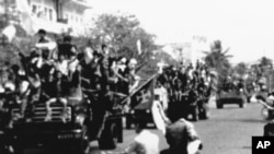 Flags waving as Red Khmer soldiers enter the city of Phnom Penh on their trucks, April 17, 1975, when this Cambodian capital surrendered to the Khmer Rouge. Civilians pass the truck convoy on their motor scooters. (AP Photo)