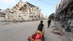 A Palestinian boy pulls a cart carrying his brother and their belongings as they flee their home during Israeli air and artillery strikes, near the site of a tower building destroyed in earlier strikes in Gaza City.