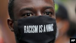 Manifestante enverga máscara facial onde se lê: Racismo é vírus