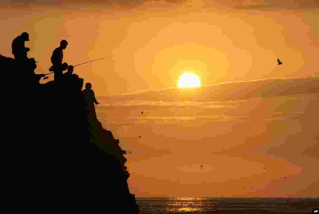 People are silhouetted while fishing during sunset at Herradura beach in Lima, Peru, Jan. 15, 2022.