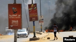 Para pengendara melintas di depan ban-ban yang dibakar sebagai penghalang di tengah demonstrasi untuk mendesak pemerintah memperbaiki kondisi negara di Khartoum, Sudan, Rabu, 21 Oktober 2020. (Foto: Reuters)