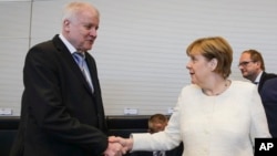 German Chancellor Angela Merkel, right, shakes hands with Interior Minister Horst Seehofer, left, as they arrive for a special faction meeting of the Christian Union parties, ahead of a debate at the German parliament in Berlin, July 3, 2018.