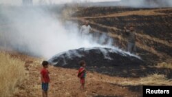 FILE - A man gestures as smoke rises from a burning farmland targeted by what activists said were airstrikes by forces loyal to Syria's President Bashar al-Assad in Maarshmarin village in Idlib countryside, May 24, 2015. 