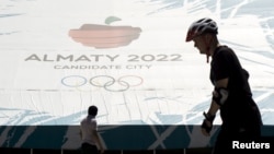 Seorang pria berjalan melewati spanduk promosi Almaty sebagai calon kota untuk penyelenggaraan Olimpiade Musim Dingin 2022 di arena olahraga skating Medeu di Almaty, Kazakhstan (26/7)