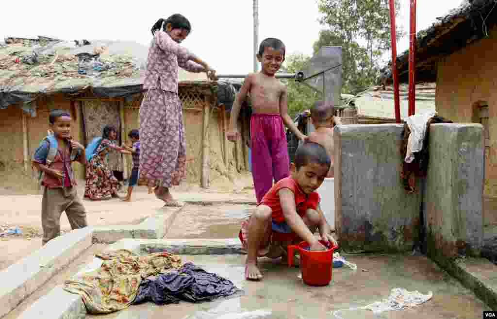 5-year-old Ayesha Siddika washes clothes while Anis Fatima, 10, pumps water up from a well at Kutupalong refugee camp Mar. 31, 2019. (Hai Do/VOA)