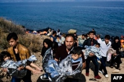 Men carry their children wrapped in emergency blankets shortly after arriving with other migrants and refugees on the Greek island of Lesbos after crossing the Aegean sea from Turkey, Oct. 18, 2015.