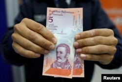 A customer shows the new five Bolivar Soberano (Sovereign Bolivar) bills, after he withdrew them from an automated teller machine at a Mercantil bank branch in Caracas, Venezuela August 20, 2018