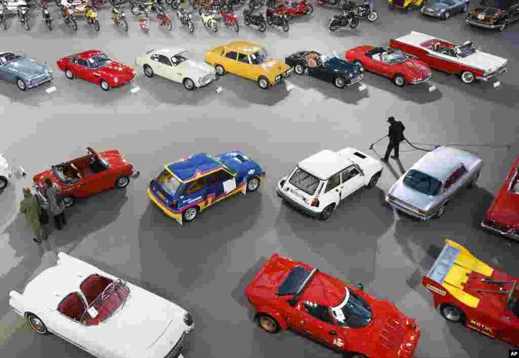 A man cleans the floor as visitors walk past vintage and classic cars displayed by Bonhams auction house, during an exhibition, at the Grand Palais in Paris, France.