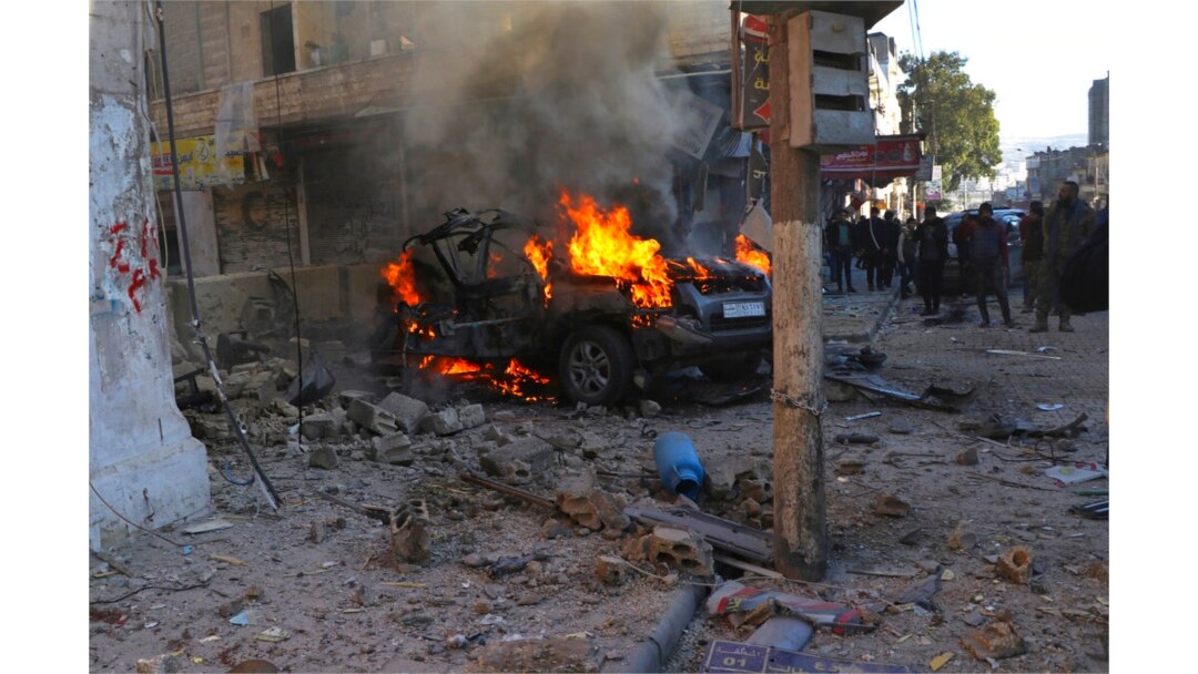 Syrians gather around a burning car hit by a shell, in the town of Afrin, north of Aleppo, Jan. 20, 2022, in this photo provided by the Syrian Civil Defense White Helmets.