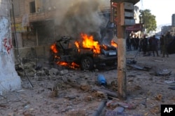 Syrians gather around a burning car hit by a shell, in the town of Afrin, north of Aleppo, Jan. 20, 2022, in this photo provided by the Syrian Civil Defense White Helmets.