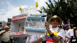 FILE - A man shows a cardboard box crafted to depict an empty refrigerator to indicate the shortage of products, during an opposition march in Caracas, Venezuela, May 14, 2016. 
