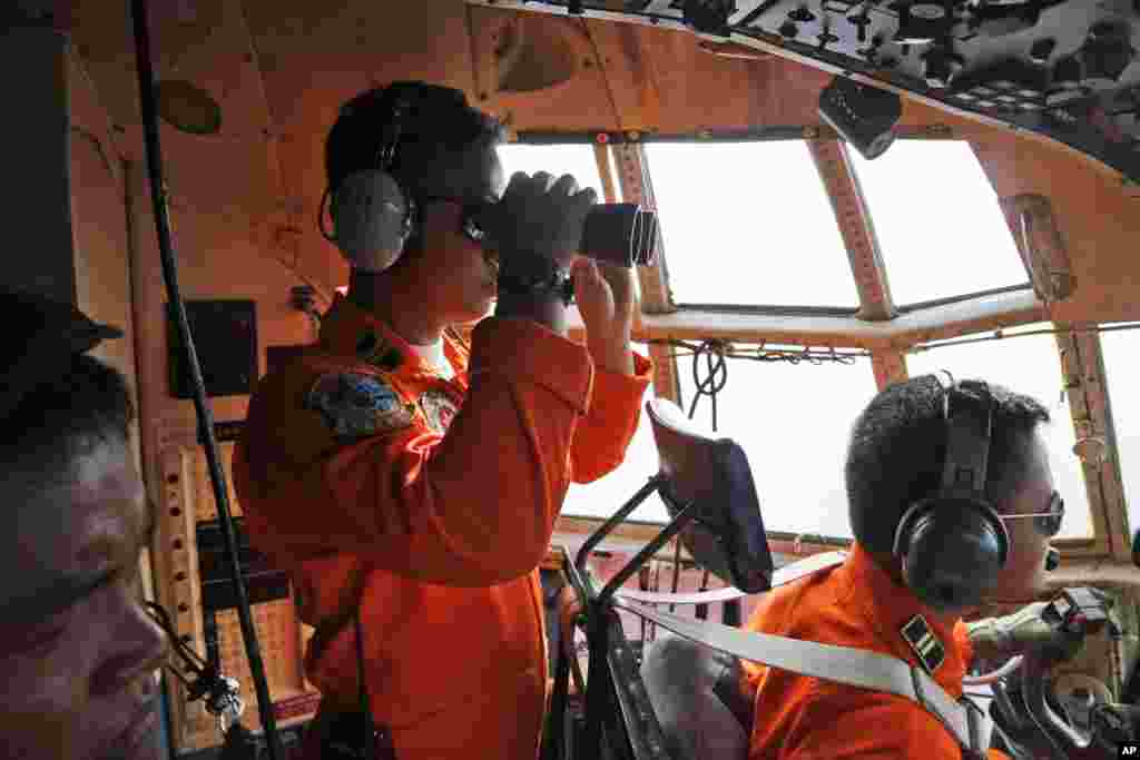 Kru pesawat TNI AU C-130 Squadron 31 menggunakan teropong untuk menelusuri cakrawala dalam operasi pencarian pesawat AirAsia 8501 yang hilang di atas perairan Selat Karimata di Indonesia, 29 Desember 2014.