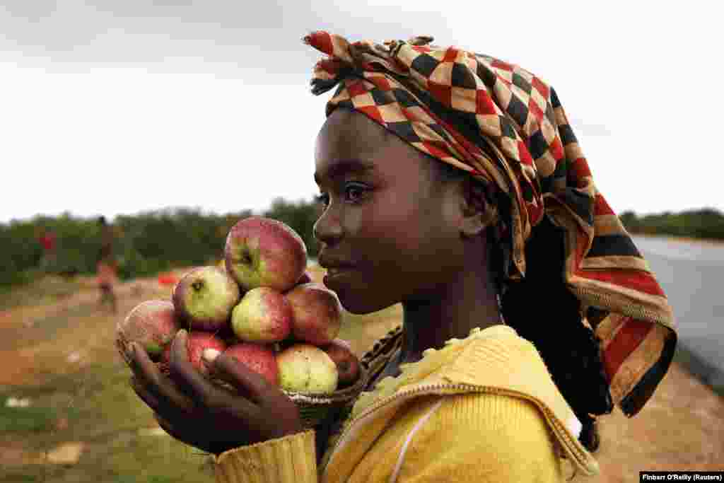 Uma menina vende maçãs nas ruas do Lubango