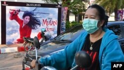 ແມ່ຍິງຄົນນຶ່ງໃສ່ໜ້າກາກ, ທ່າມກາງຄວາມເປັນຫ່ວງ ກ່ຽວກັບ ການແຜ່ລາມຂອງໄວຣັສໂຄໂຣນາສາຍພັນໃໝ່, ຂັບລົດຈັກຜ່ານປ້າຍໂຄສະນາຮູບເງົາ ມູລານ ໃນນະຄອນຫຼວງ ວຽງຈັນ, 11 ມີນາ, 2020. (Photo by Mladen ANTONOV / AFP)