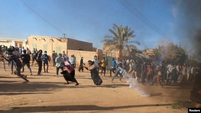 FILE - Sudanese demonstrators run from a teargas canister fired by riot policemen to disperse them as they participate in anti-government protests in Omdurman and Khartoum, Sudan, Jan. 20, 2019.