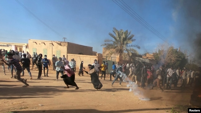 FILE - Sudanese demonstrators run from a teargas canister fired by riot policemen to disperse them as they participate in anti-government protests in Omdurman and Khartoum, Sudan, Jan. 20, 2019.