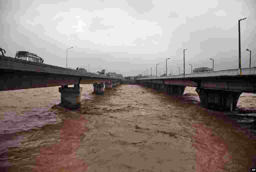 People ride their vehicles in a bridge across a river flooded following monsoon rains in Jammu, India, Sept. 5, 2014.