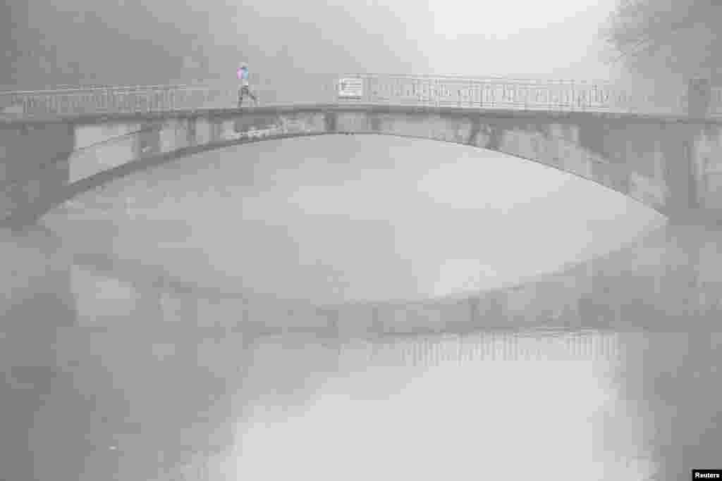 A woman runs over a bridge crossing the Isar river covered in fog in Munich, Germany.