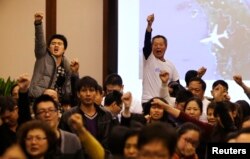 Family members of passengers onboard Malaysia Airlines Flight MH370 raise their fists as they shout "return our families" to protest against the lack of new information after a routine briefing given by Malaysia's government and military representatives at Lido Hotel in Beijing, Mar. 22, 2014.