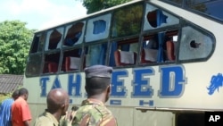 A Kenyan police officer with civilians views a Taheed Bus at the Lamu Police Station in Lamu, July 19, 2014. 